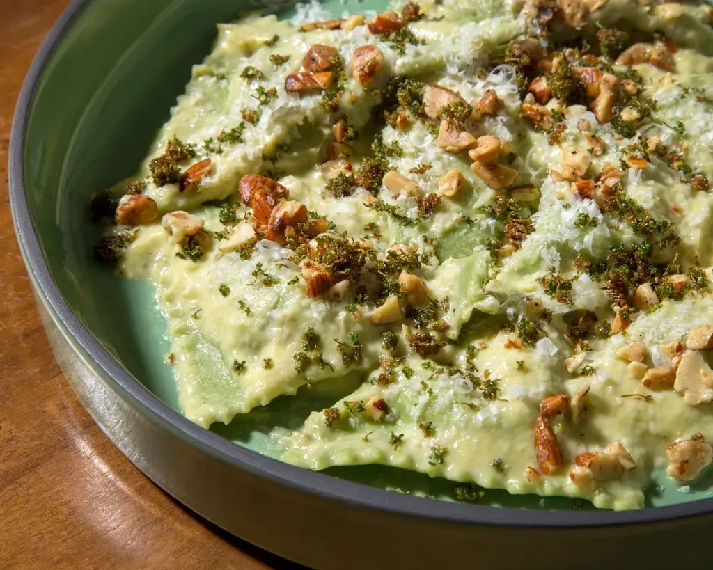 Close-up of pasta with creamy sauce, herbs, nuts, and seasoning.