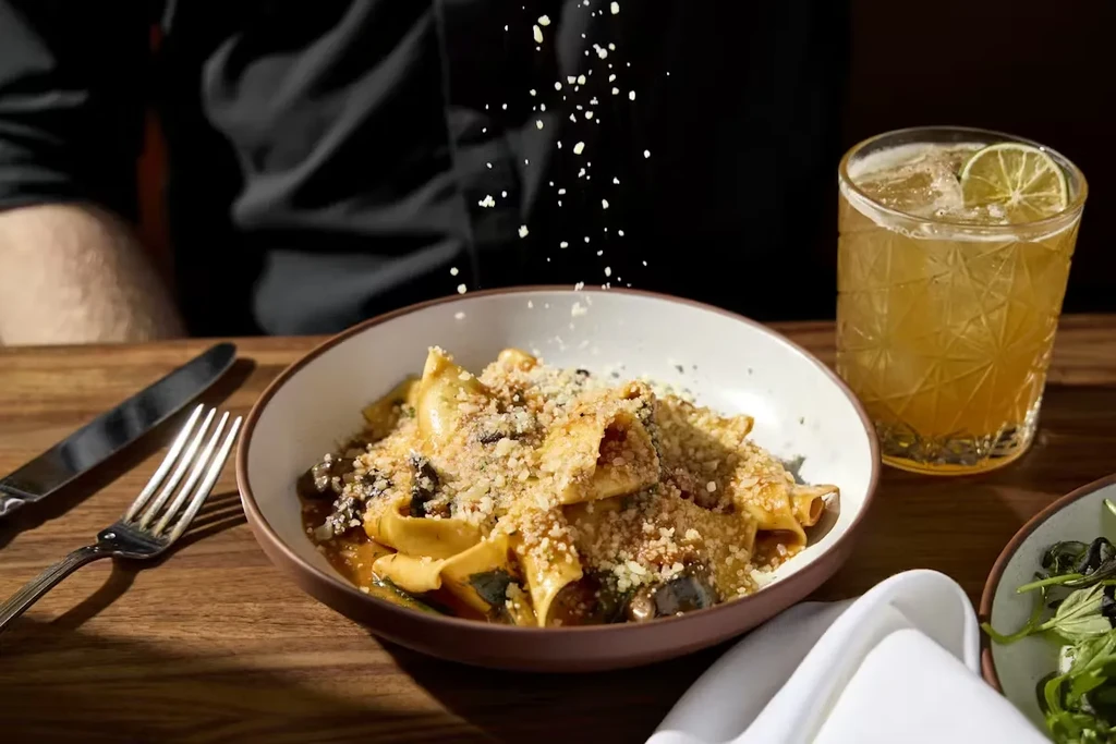 Close-up of pasta with dark sauce, garnished with falling grated cheese.