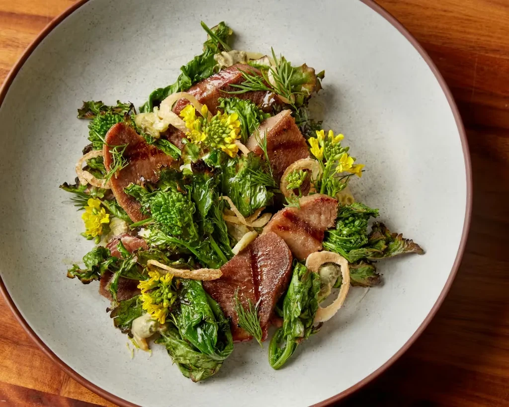 Gourmet dish with grilled meat, green vegetables, and crispy onions.