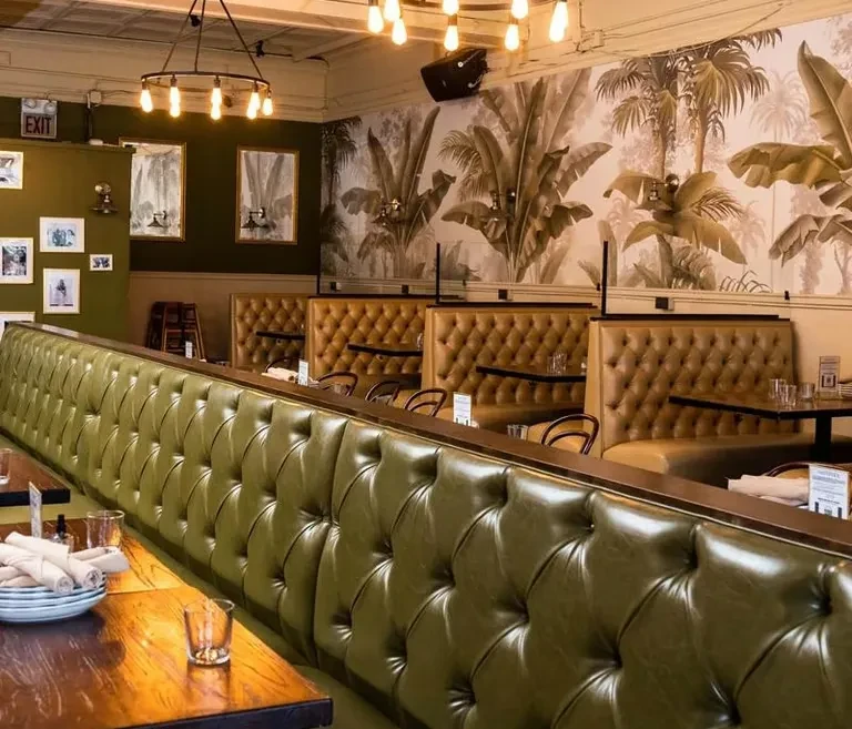 Restaurant interior with olive-green tufted leather bench and tropical wallpaper.