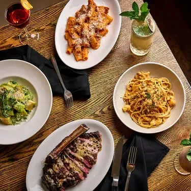 Overhead view of a wooden dining table laden with five pasta dishes.