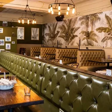 Restaurant interior with green banquette, brown booths, and tropical wallpaper.