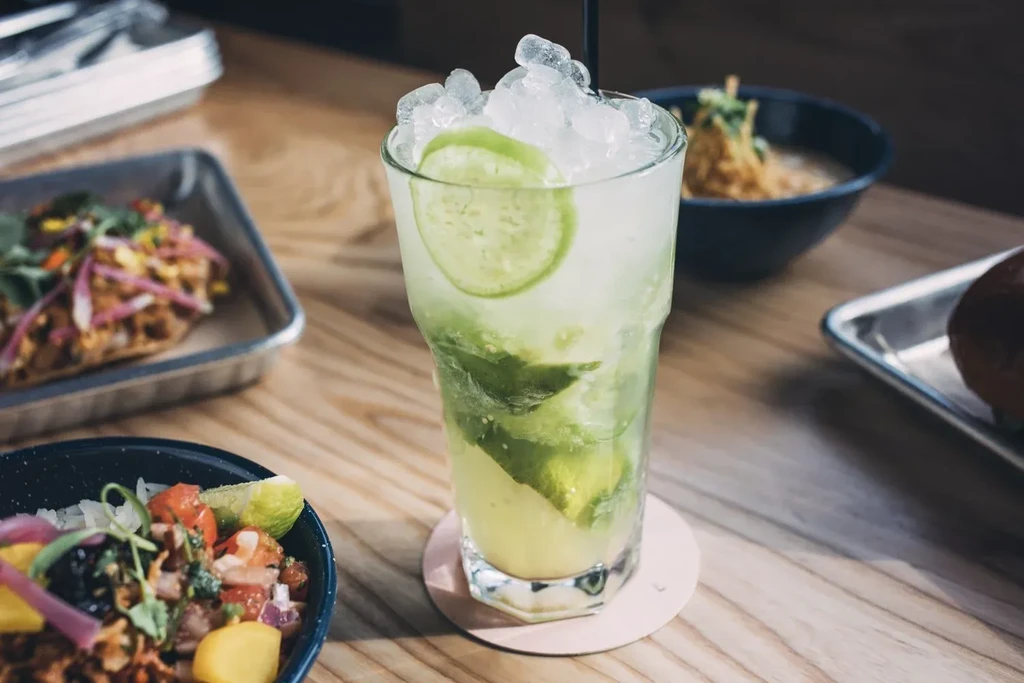 Tall green drink with crushed ice and lime on a wooden table.