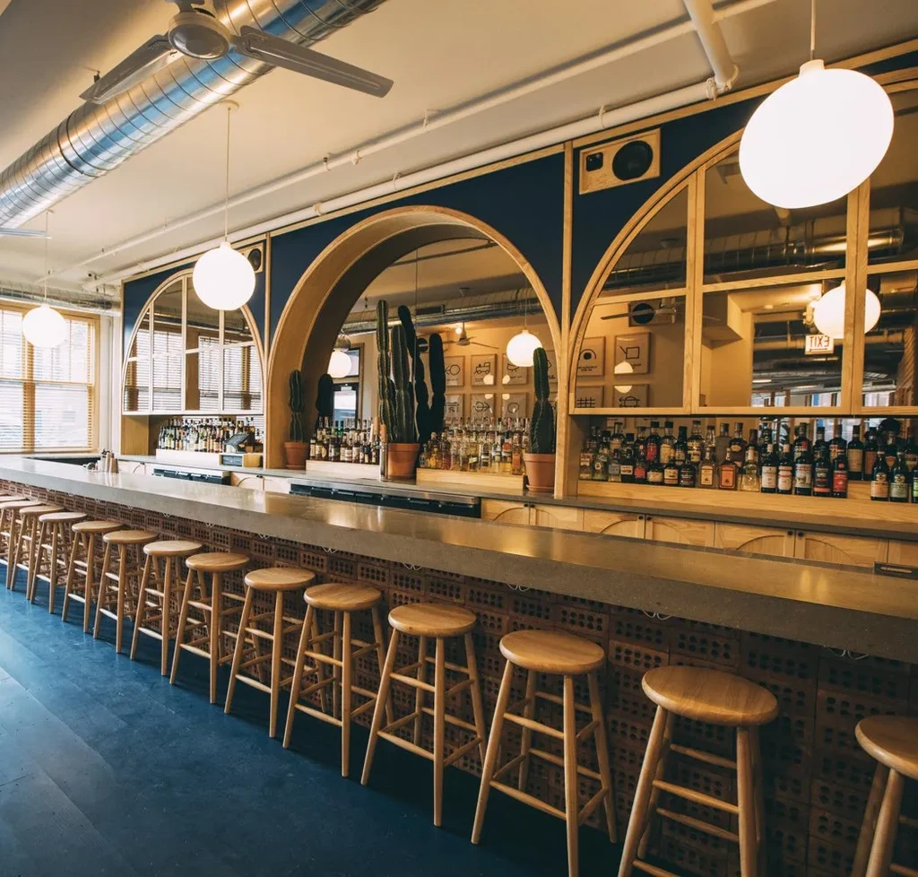 Empty bar interior with brick counter, patterned wall, and potted cacti.