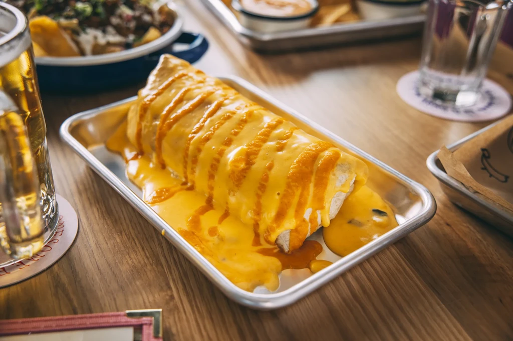 Cheese-covered burrito in a metal tray on a wooden table.