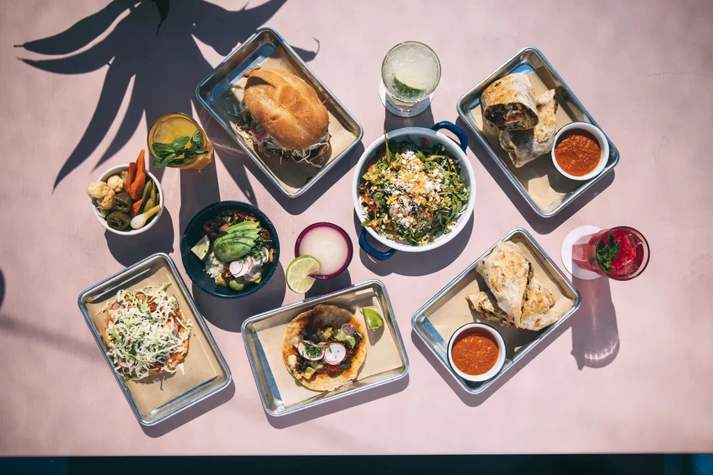 Overhead shot of various Mexican dishes and drinks on a pink table.