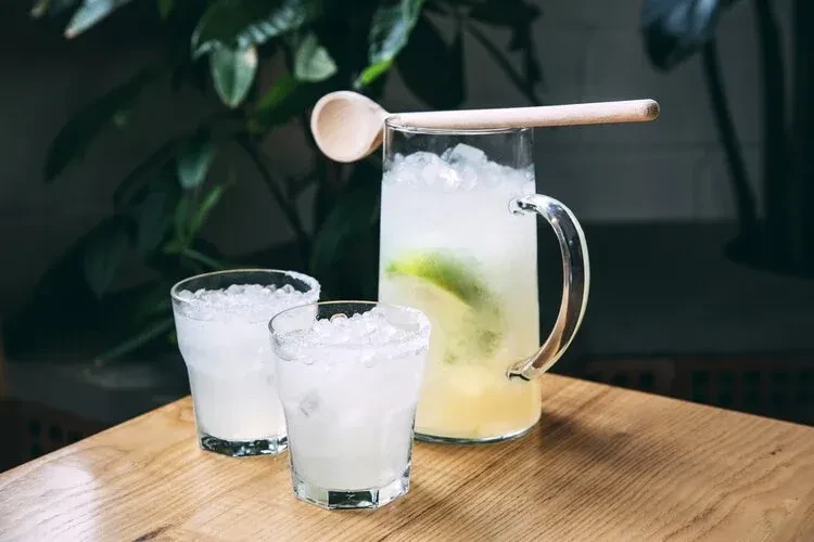 Pitcher and two glasses of a light yellow drink with lime.