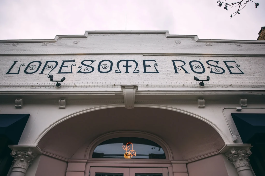 Exterior of LONESOME ROSE building with orange neon plant sign.