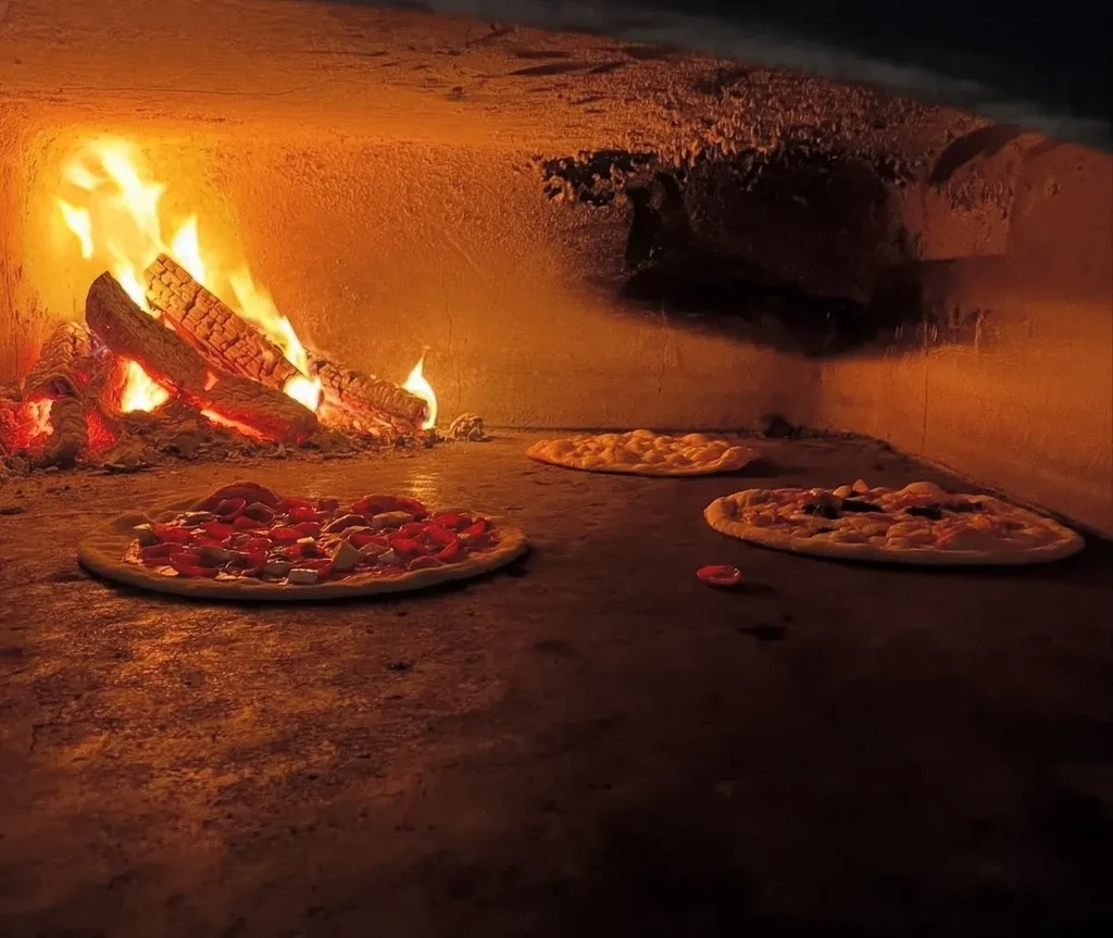 Wood-fired oven interior with active flames and three pizzas baking.