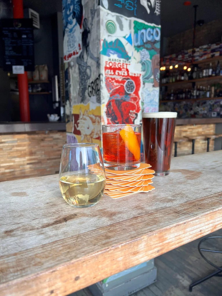 Three drinks on a rustic wooden bar with posters in background.