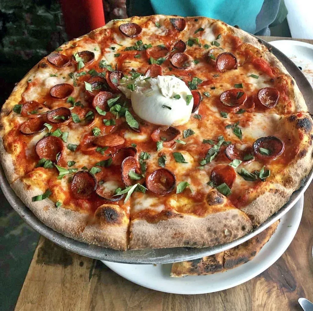 Pepperoni pizza with basil and burrata on a wooden table.
