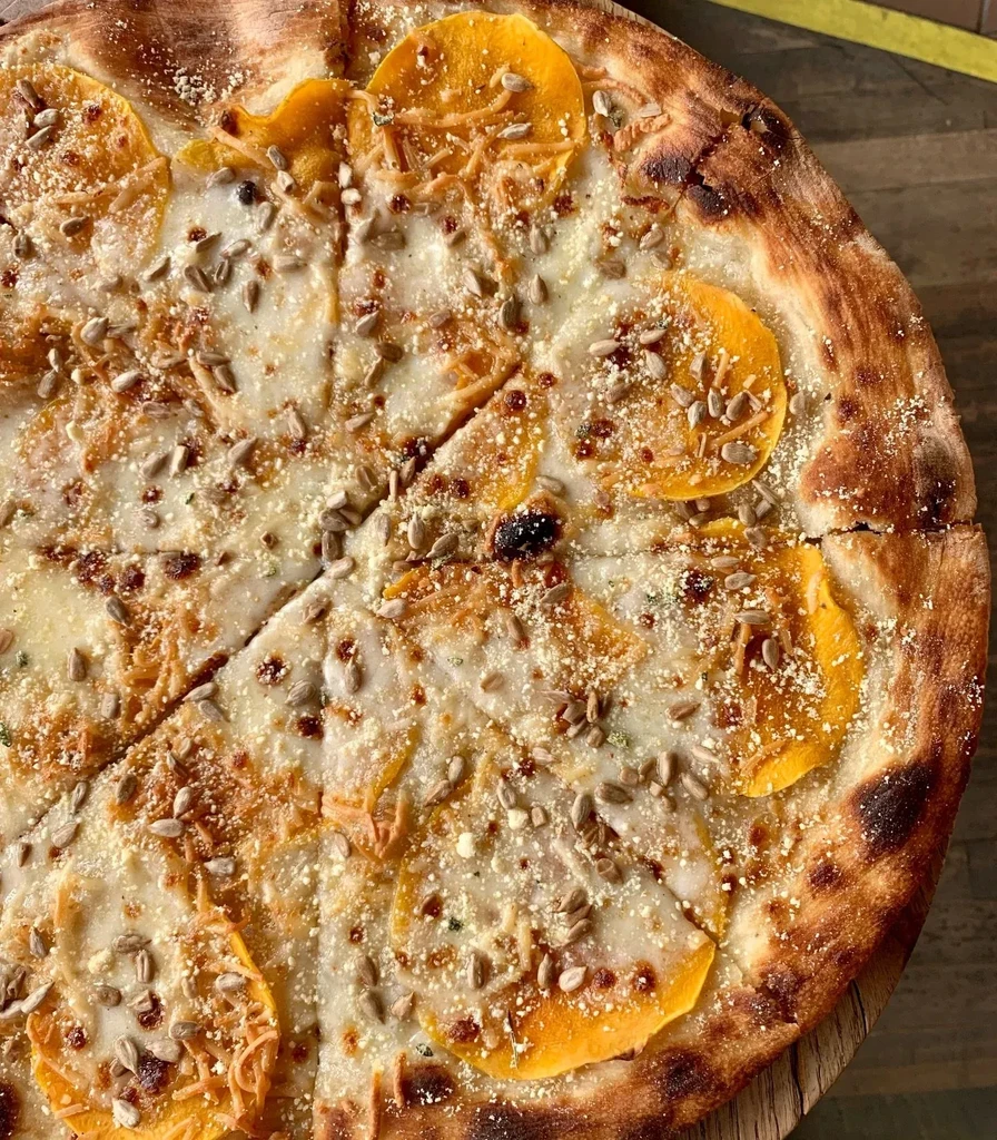 Round pizza with melted cheese, sunflower seeds, and orange slices.