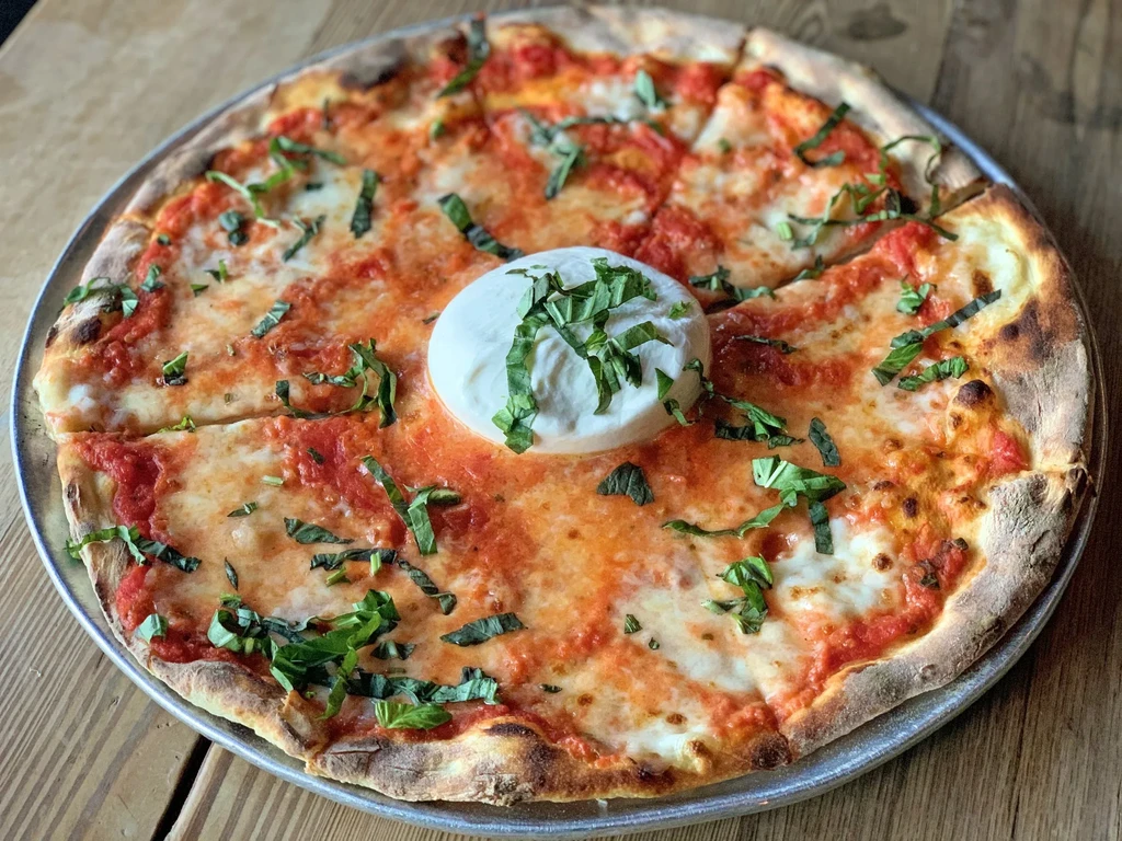 Overhead shot of a pizza with burrata, basil, and charred crust.
