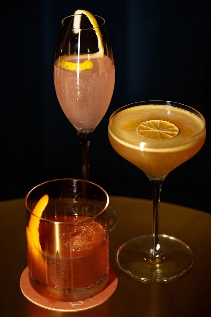Three cocktails, garnished with citrus, on a reflective surface.