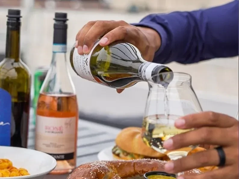 Hands pouring white wine from a green bottle into a glass.