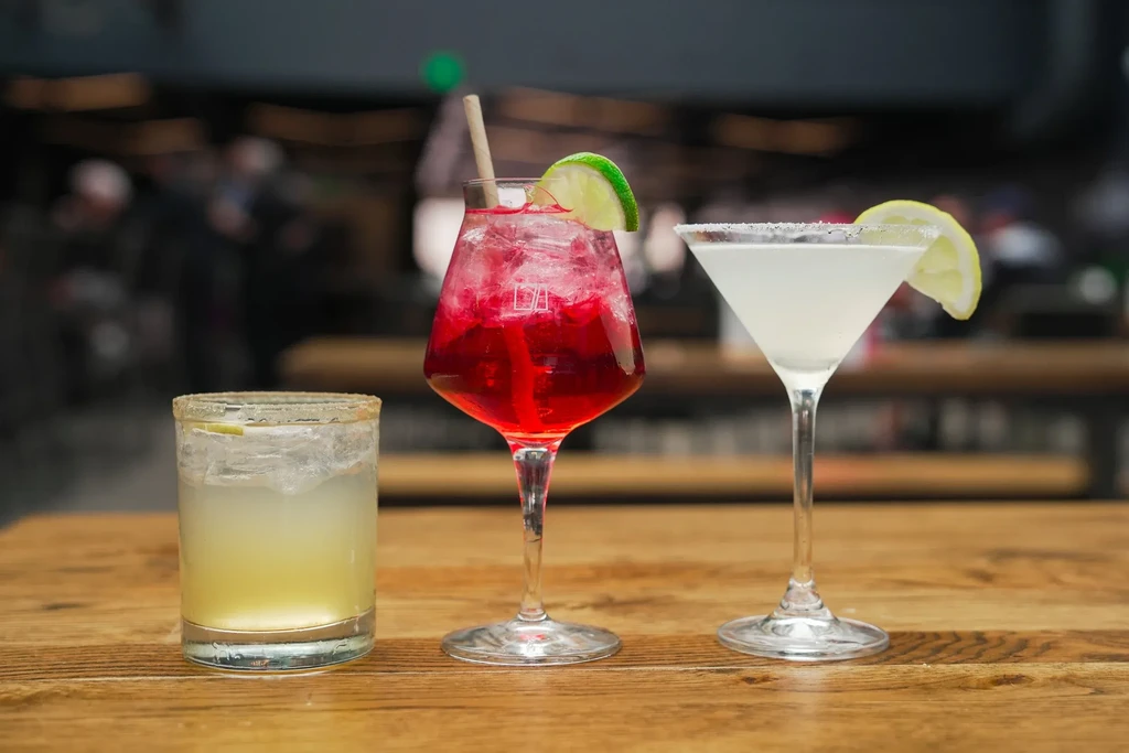 Three distinct alcoholic beverages are displayed on a rustic wooden table.