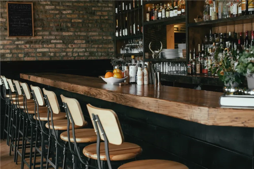Stylish empty bar with wooden counter, brick wall, and liquor bottles.