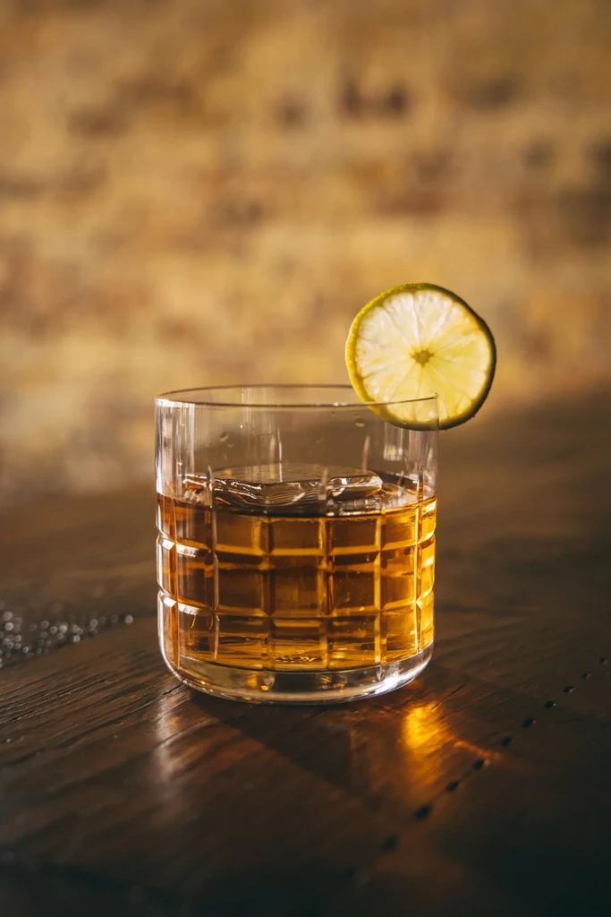 Whiskey with a square ice cube and lime slice.