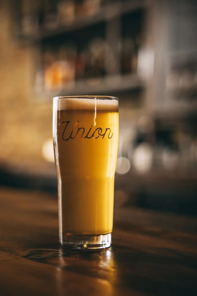 Pint glass of amber beer with foam, word "Union" on glass.