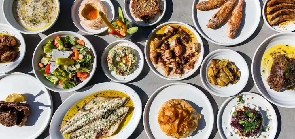 Top-down view of many plates of various foods on a grey surface.