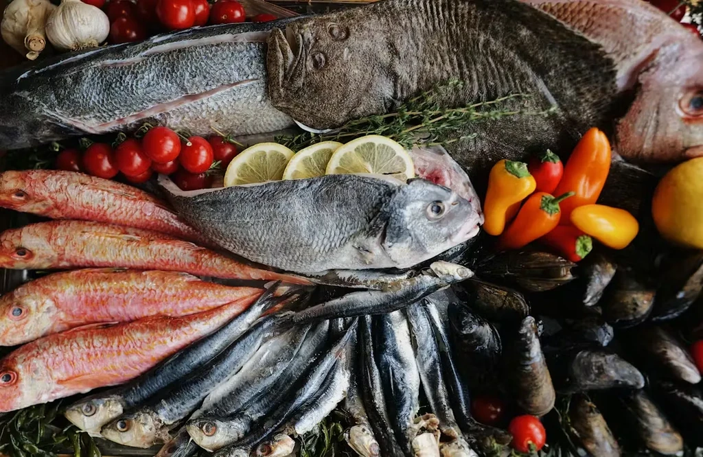 Assortment of fresh fish, mussels, tomatoes, lemons, garlic, and herbs.