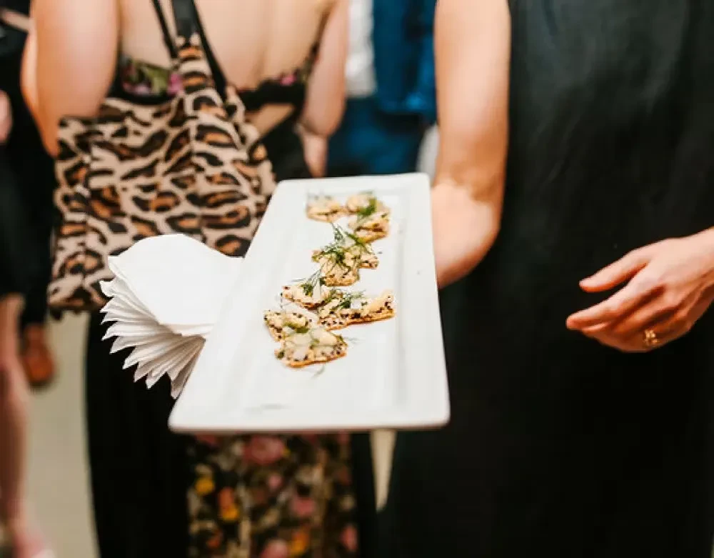 Arm holding white platter of appetizers garnished with green herbs.