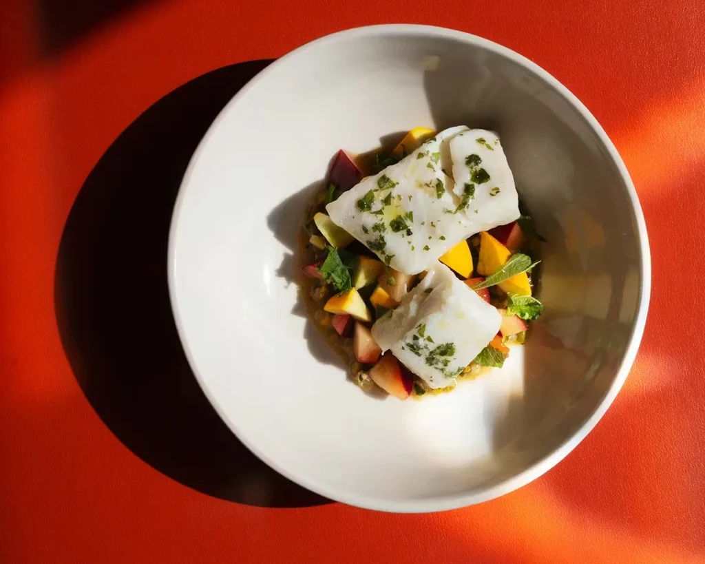 Fish garnished with herbs on colorful fruit and vegetable salsa.
