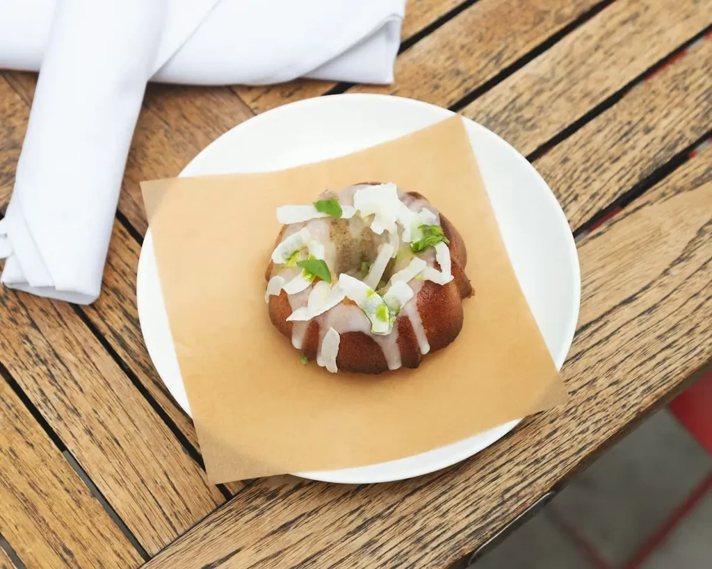 Dark brown bundt cake with white icing, coconut, and green specks.