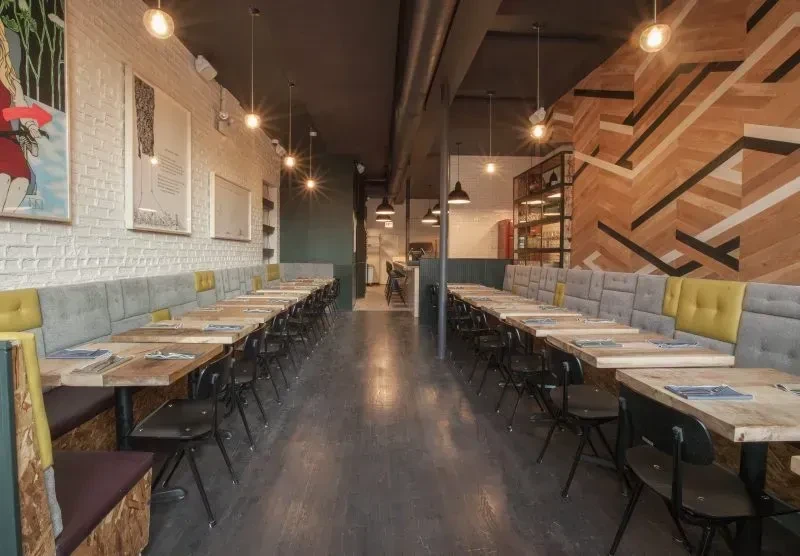 Modern restaurant interior with long rows of tables, benches, and accent walls.