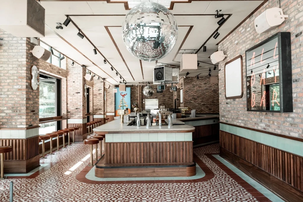 Modern bar interior with disco balls, brick walls, and patterned floor.