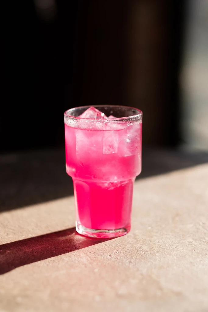 Pink drink with ice in a clear, textured glass.
