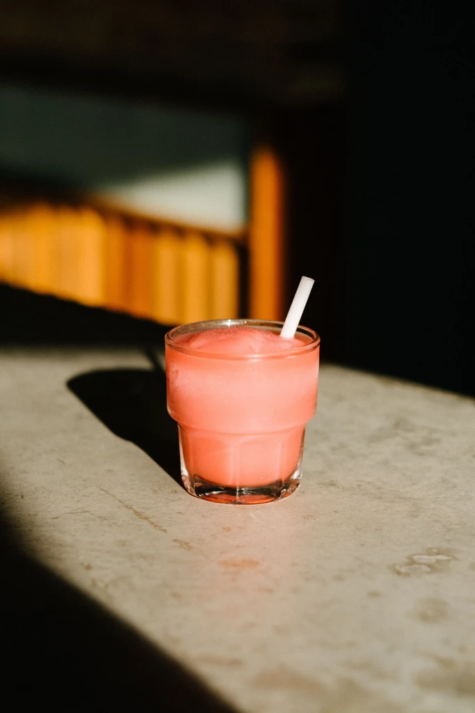 Pink frozen drink in a glass with a straw on a textured surface.