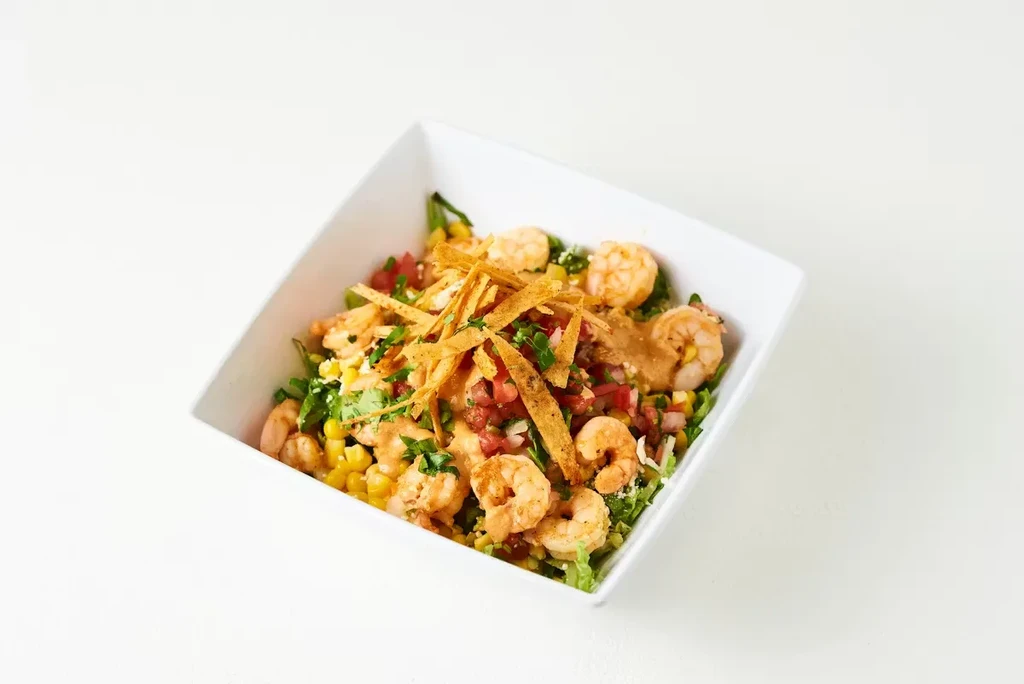 Shrimp salad with lettuce, corn, tomatoes, tortilla strips, and herbs.