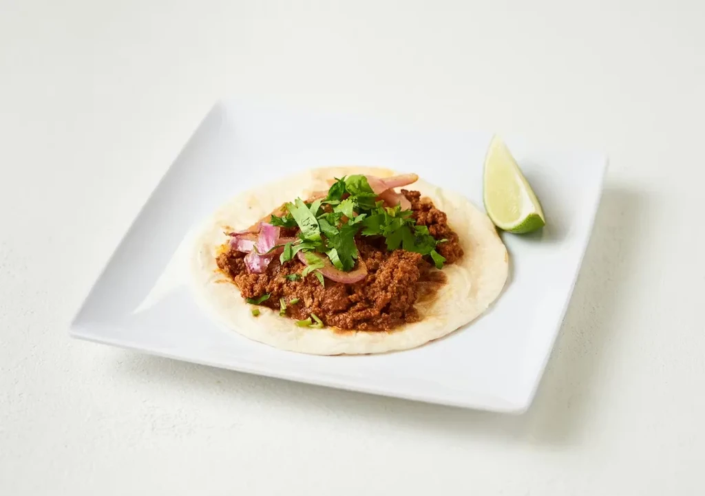 Soft taco with ground meat, cilantro, red onion, and lime.