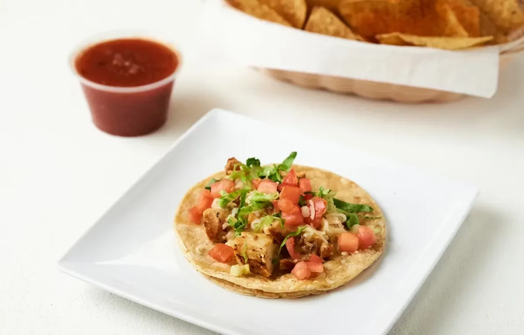 Single taco on white plate with salsa and chips.