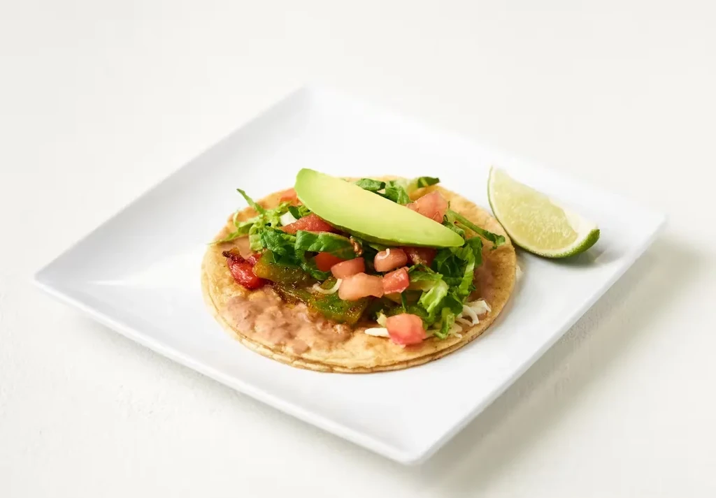 Tostada with beans, lettuce, tomatoes, peppers, avocado, and lime.
