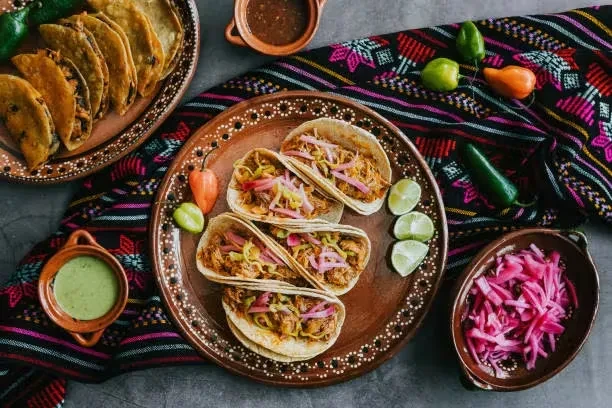 Overhead shot of two plates of tacos with sauces, limes, and peppers.
