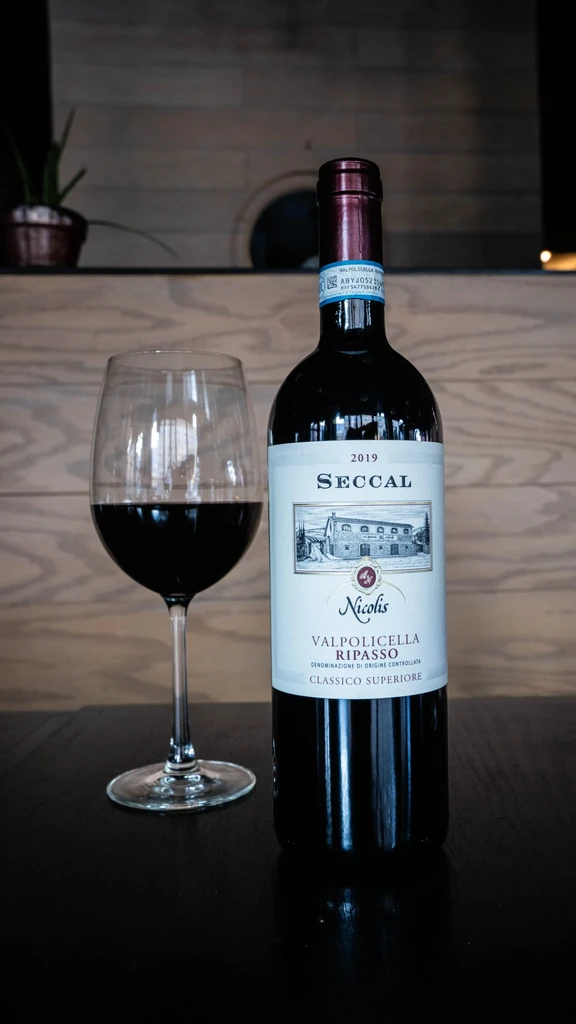 Bottle of red wine and half-filled glass on a reflective surface.
