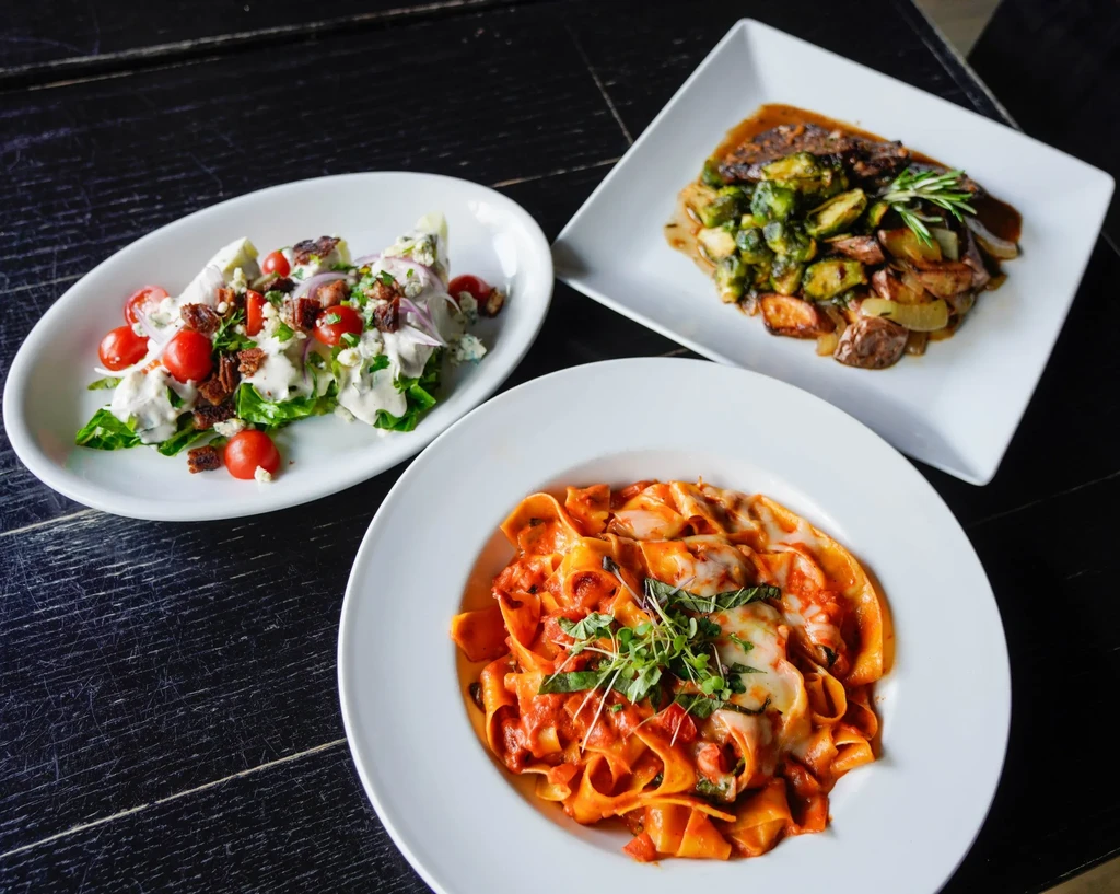 Three plated dishes: pasta, wedge salad, and meat with vegetables.