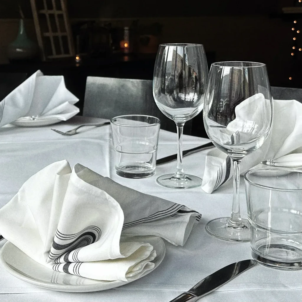 Restaurant table set with white plates, napkins, and glassware.