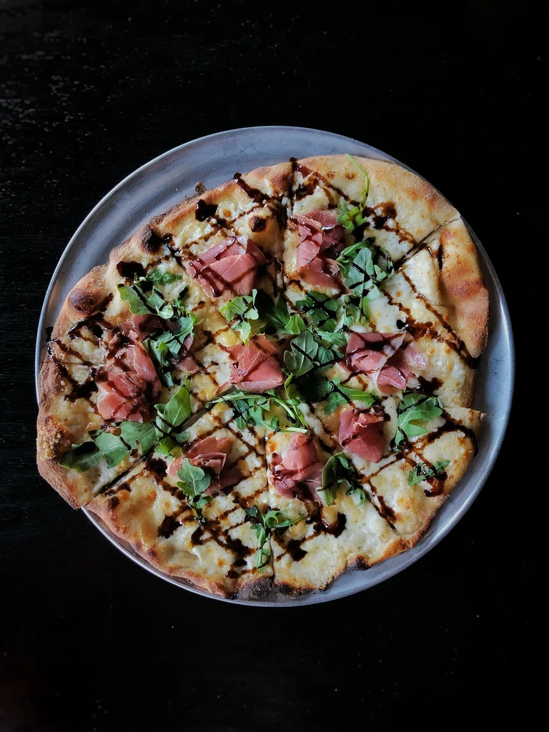 Pizza with white cheese, prosciutto, arugula, and balsamic glaze.