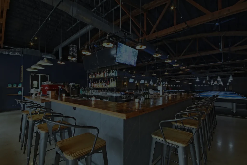 Modern bar interior with a wrap-around bar, liquor shelves, and pool tables.