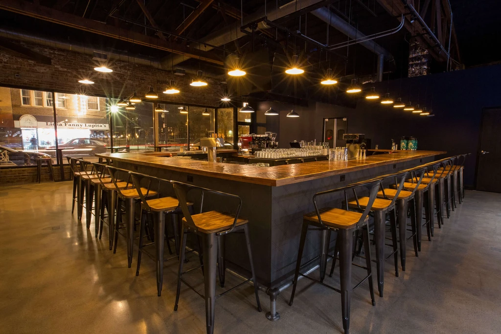 Empty bar with L-shaped counter, stools, and exposed brick walls.