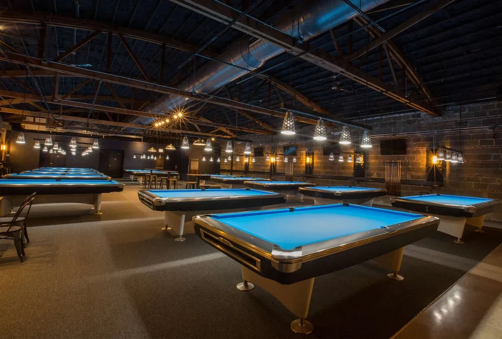 Dimly lit hall with many blue-felted pool tables.