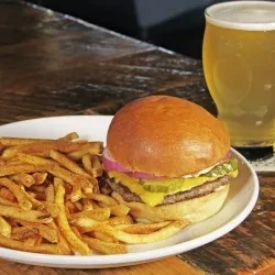 Burger, fries, and a partial glass of beer on a wooden table.