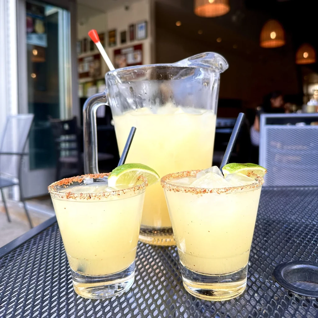 Pitcher and two glasses of icy yellow drinks with lime.