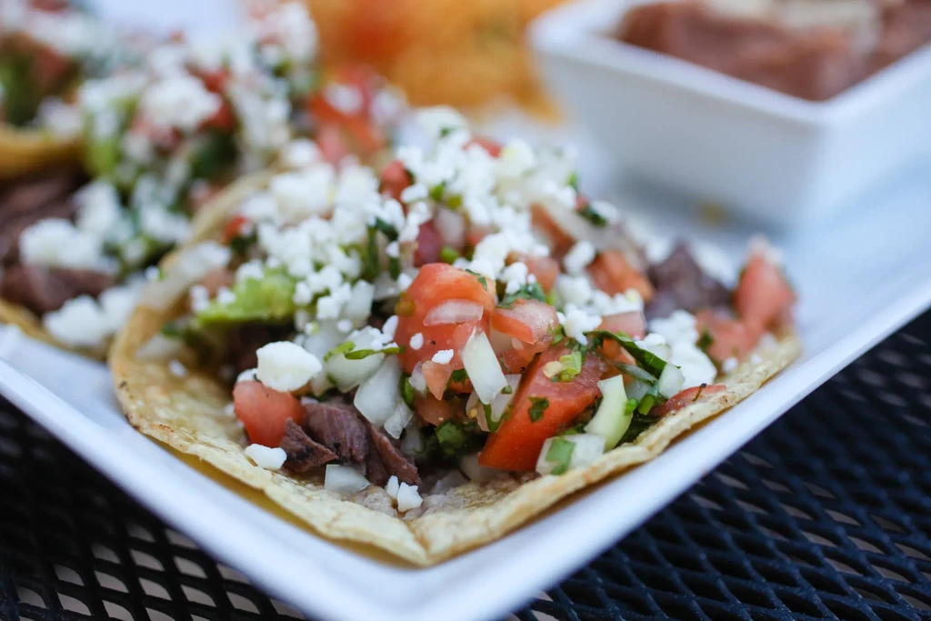 Close-up of three street tacos with pico de gallo and cheese.