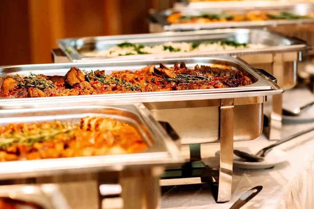 Buffet setup with a chafing dish of meat garnished with herbs.