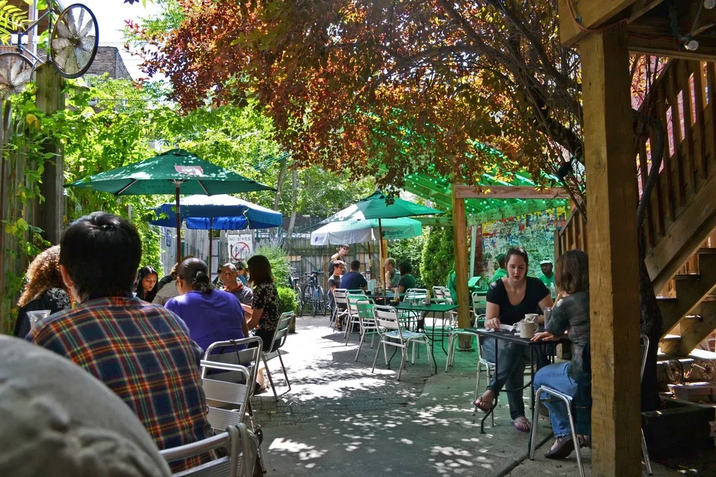 People seated at outdoor tables under umbrellas and trees.