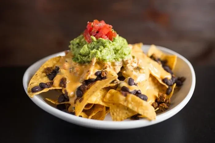 Close-up of nachos with cheese, guacamole, tomatoes, and beans.